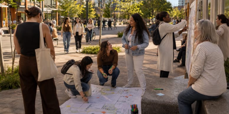 Women taking part in an outdoor urban planning activity with maps, drawings and a public display board.